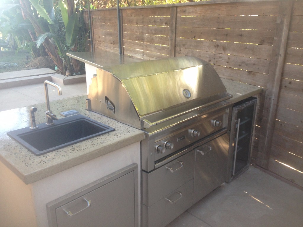 Backyard BBQ setup with concrete countertops and custom sink and fridge storage